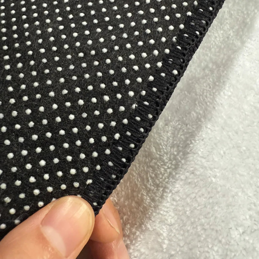 Back edge detail of rug with black overlock stitching and dotted non-slip backing.