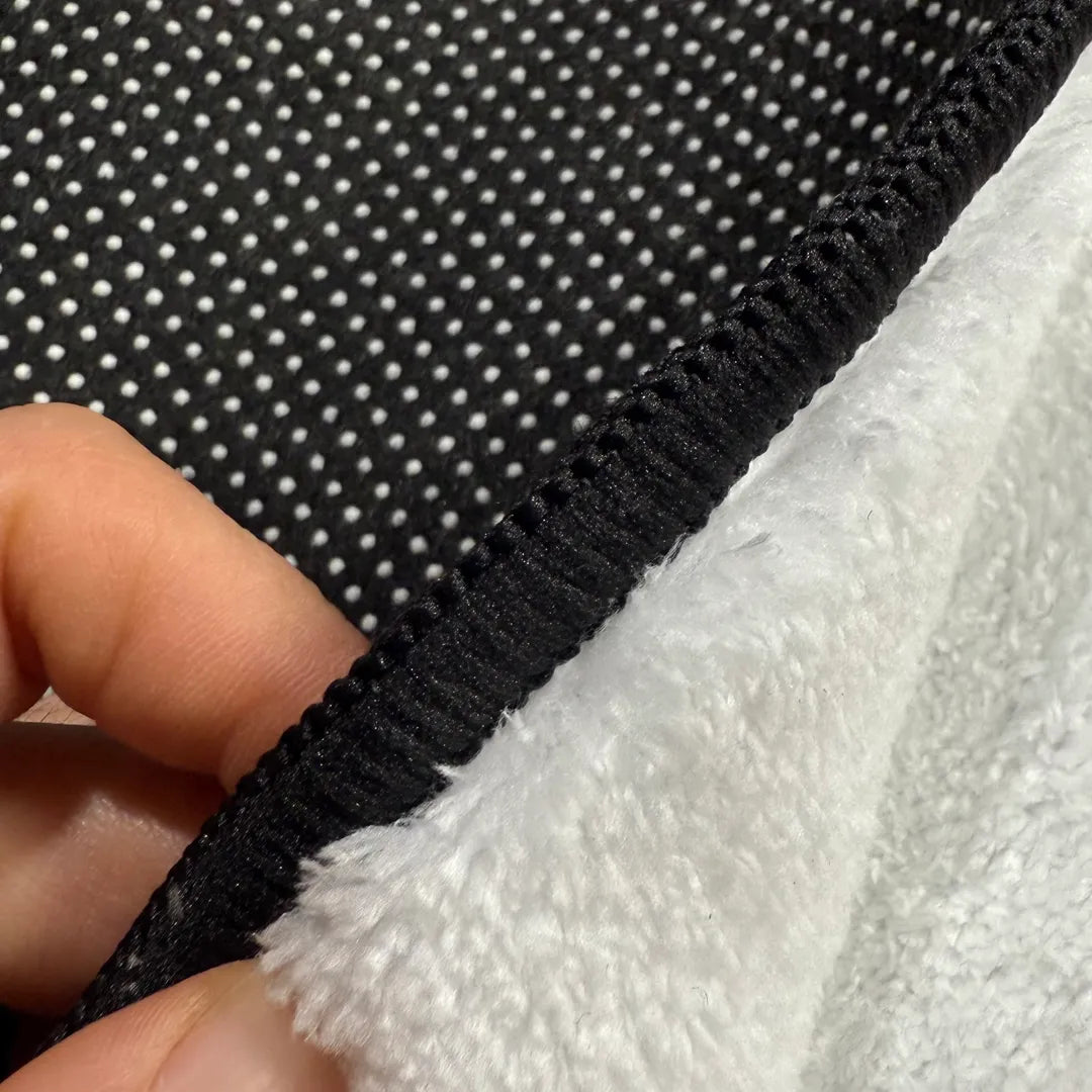 Front edge detail of rug with black overlock stitching framing the faux cashmere surface.