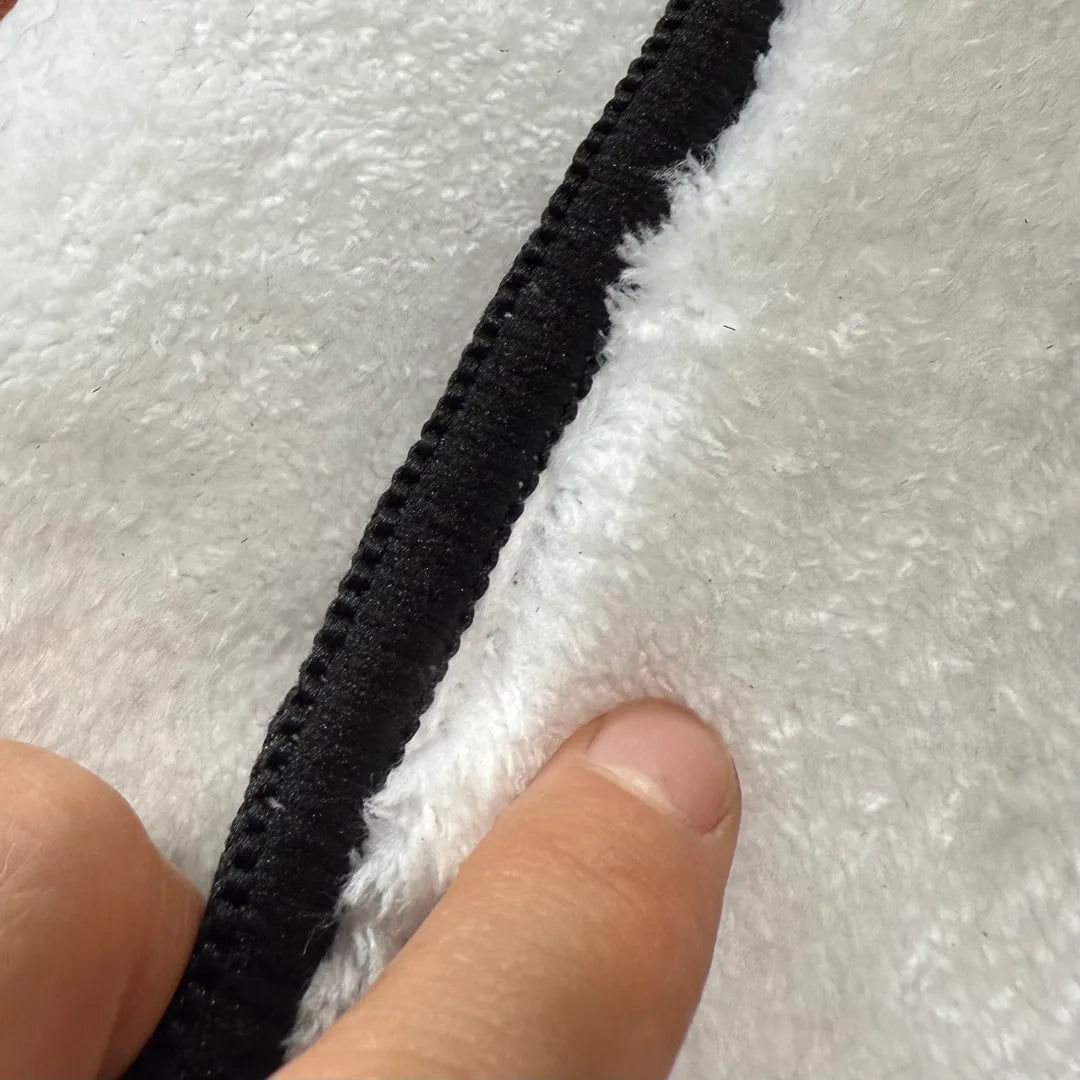 Front edge detail of rug with black overlock stitching framing the faux cashmere surface.