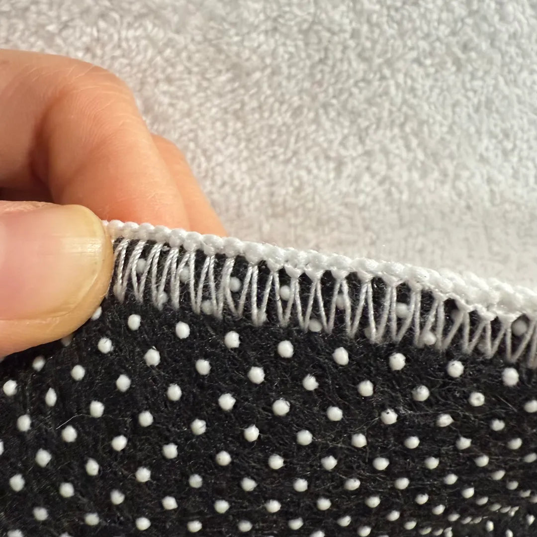 Back edge detail of rug with warm white overlock stitching and dotted non-slip backing.