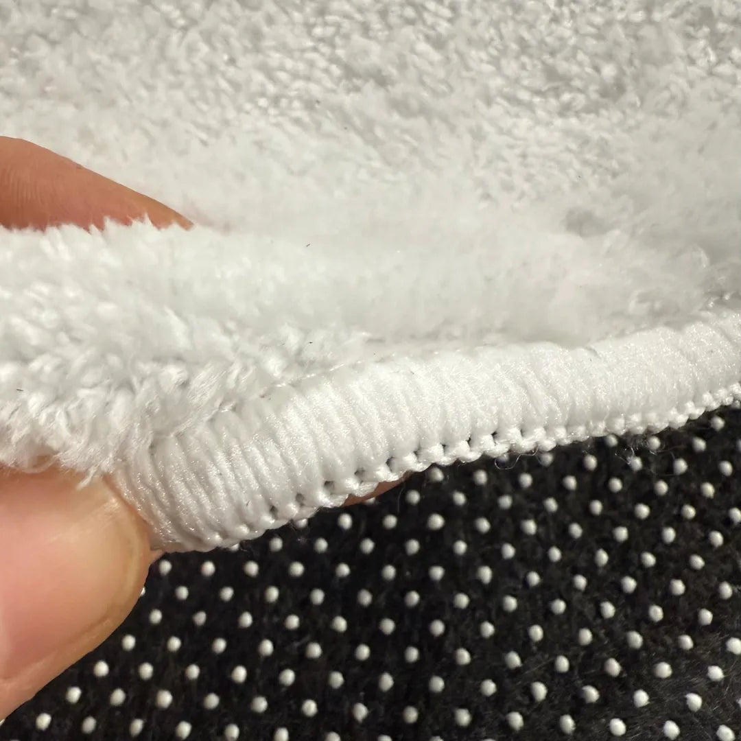 Front edge detail of rug with warm white overlock stitching on faux cashmere surface.