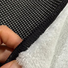 Front edge detail of rug with black overlock stitching framing the faux cashmere surface.