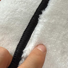 Front edge detail of rug with black overlock stitching framing the faux cashmere surface.