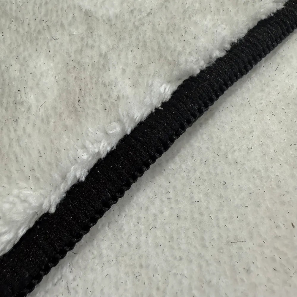 Front edge detail of rug with black overlock stitching framing the faux cashmere surface.