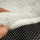 Front edge detail of rug with warm white overlock stitching on faux cashmere surface.