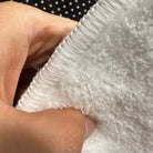 Front edge detail of rug with warm white overlock stitching on faux cashmere surface.