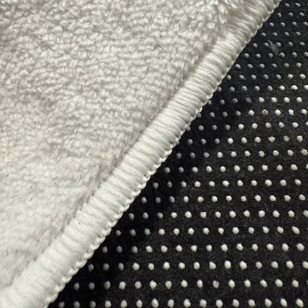 Front edge detail of rug with warm white overlock stitching on faux cashmere surface.